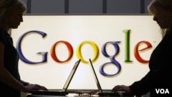 Exhibitors work in front of an illuminated sign of the Google logo in Hanover, Germany